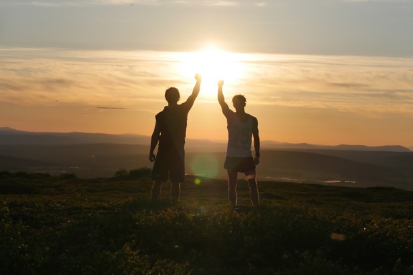 Två personer står i motljus och håller upp händerna mot varandra.