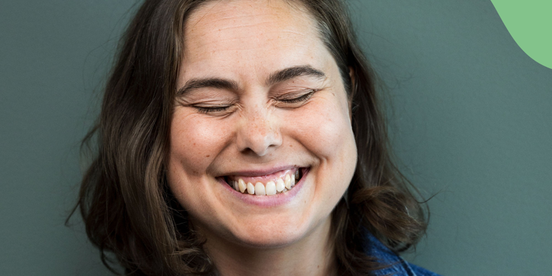 Fotografi av Agnes Török. Hen står mot en grön bakgrund och ler stort och blundar på bilden. Hen har axellångt mörkt hår och en blå skjorta på sig. I bildens högra övre hörn sysn en grön målad våg. Text i bild: Agens Török Sveriges Läsambassadör