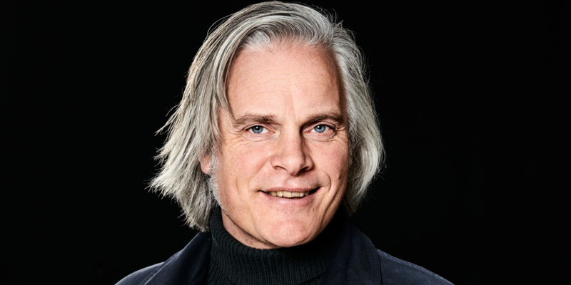 Porträttbild på Tobias Barenthin Lindblad mot en svart bakgrund. Tobias har på sig mörka kläder och tittar in i kameran. Han har ljust mellanlångt grått hår i sidbena och ler. Ovanför Tobias syns texten "Graffiti Smak och juridik - konst eller skadegörelse?"