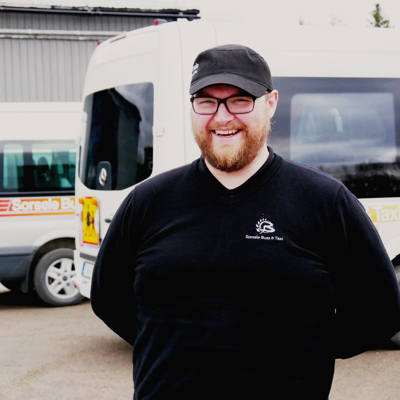 Oscar Öjeryd står och ler framför tre parkerade minibussar.