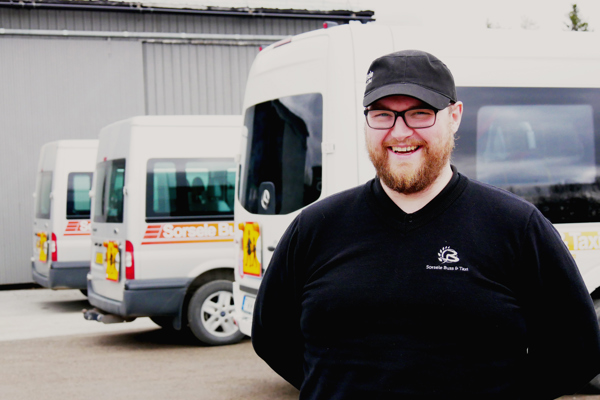 Oscar Öjeryd står och ler framför tre parkerade minibussar.