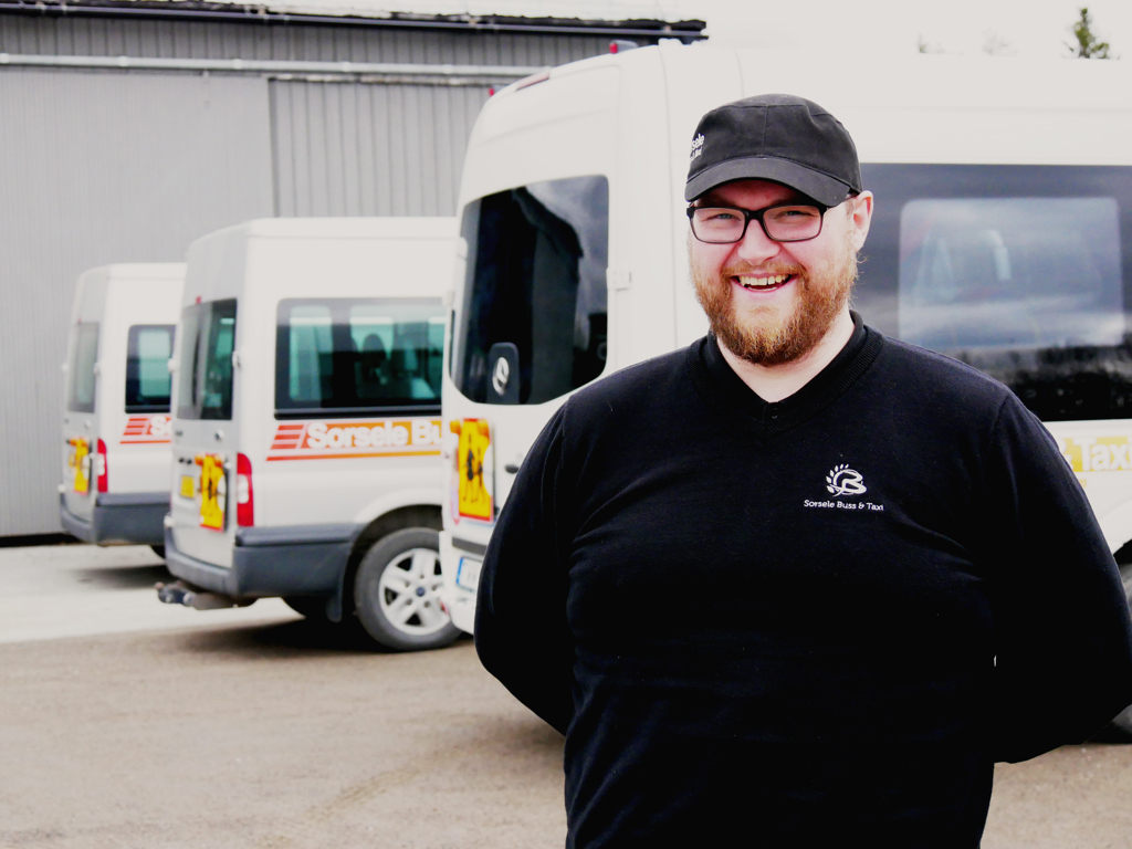 Oscar Öjeryd står och ler framför tre parkerade minibussar.